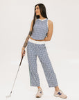 A person standing wearing the Bronson Pant in indigo color, which features a geometric pattern. The pants are casual and the person is paired them with a matching top and pink sneakers.