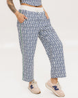 A person standing wearing the Bronson Pant in indigo color, which features a geometric pattern. The pants are casual and the person is paired them with a matching top and pink sneakers.