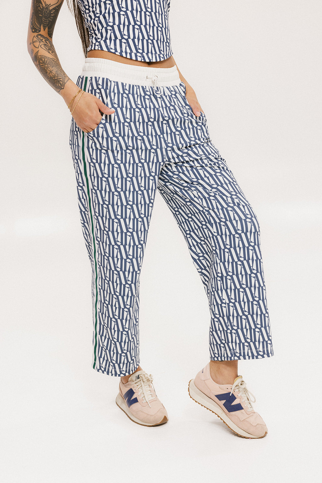 A person standing wearing the Bronson Pant in indigo color, which features a geometric pattern. The pants are casual and the person is paired them with a matching top and pink sneakers.