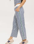 A person standing wearing the Bronson Pant in indigo color, which features a geometric pattern. The pants are casual and the person is paired them with a matching top and pink sneakers.