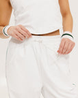 A pair of white Bronson pants with a subtle stripe detail on the side, paired with a white top and pink sneakers.