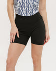 A person wearing black mid-thigh length shorts, called Biddy Shorties, with a blue and white geometric patterned top.