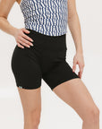 A person wearing black mid-thigh length shorts, called Biddy Shorties, with a blue and white geometric patterned top.