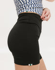 A person wearing black mid-thigh length shorts, called Biddy Shorties, with a blue and white geometric patterned top.