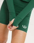A pair of green mid-rise shorts with a logo on the left leg, worn with a matching green crop top.