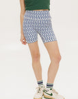 A pair of blue and white geometric shorts, knee-length, worn by a model paired with a green top and white sneakers.
