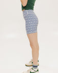 A pair of blue and white geometric shorts, knee-length, worn by a model paired with a green top and white sneakers.