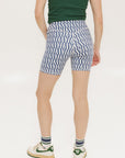 A pair of blue and white geometric shorts, knee-length, worn by a model paired with a green top and white sneakers.