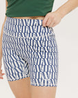 A pair of blue and white geometric shorts, knee-length, worn by a model paired with a green top and white sneakers.