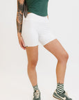 A person wearing white biddy shorties paired with a green lillee tank.