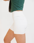 A person wearing white biddy shorties paired with a green lillee tank.