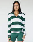 A woman wearing a green and white striped sweater with a V-neck collar and a small embroidered logo on the chest.