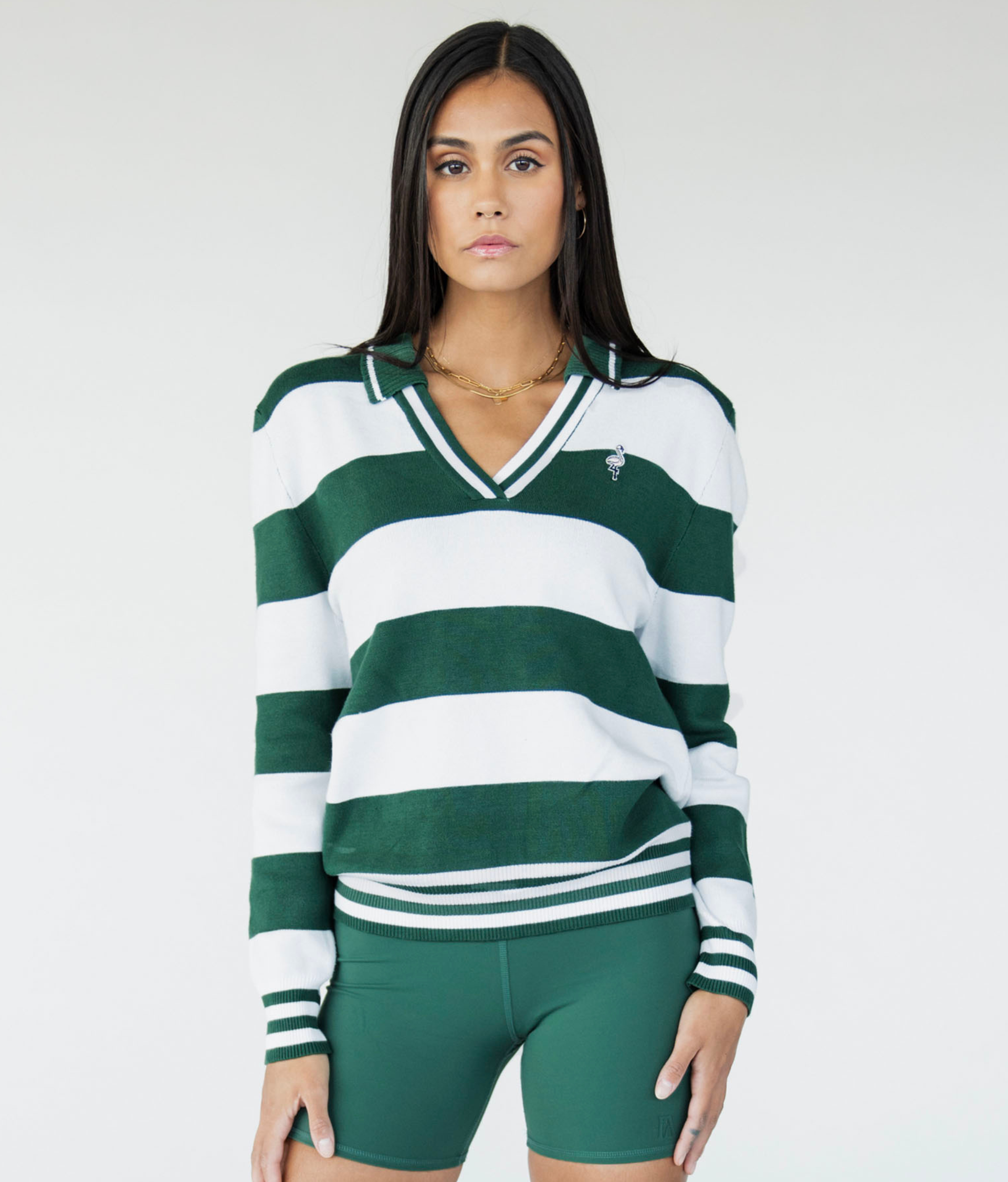 A woman wearing a green and white striped sweater with a V-neck collar and a small embroidered logo on the chest.