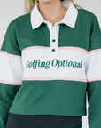 A woman wearing a long sleeve polo shirt with green, white, and pink colors, featuring the text 'Golfing Optional' on the front.