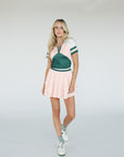 A woman wearing a pink and green Betty Polo shirt with chevron print and a preppy collar, paired with a light pink skirt.
