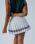 Person wearing a green top and white pleated skirt with stripes on a plain background