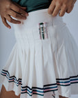 White pleated skirt with blue stripes worn by a person on a plain background