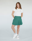 A woman wearing a white golf polo with a collar and a green skirt.