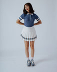 A woman wearing a blue polo shirt with a unique, preppy collar and white striped sleeves, paired with a white skirt.