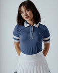 A woman wearing a blue polo shirt with a unique, preppy collar and white striped sleeves, paired with a white skirt.