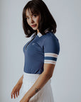 A woman wearing a blue polo shirt with a unique, preppy collar and white striped sleeves, paired with a white skirt.