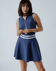 A woman wearing a navy blue ribbed golf dress with a high collar and short sleeves, featuring a full zipper in the front.