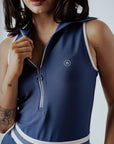 A woman wearing a navy blue ribbed golf dress with a high collar and short sleeves, featuring a full zipper in the front.