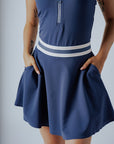 A woman wearing a navy blue ribbed golf dress with a high collar and short sleeves, featuring a full zipper in the front.