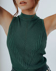 A woman wearing a green sleeveless tank top with a crew neckline and striped pants.