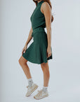 A model wearing a green knee-length skirt with a tie-belt and shorties underneath. The skirt has a textured fabric.