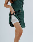 A model wearing a green knee-length skirt with a tie-belt and shorties underneath. The skirt has a textured fabric.