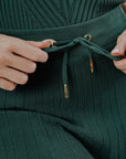 A model wearing a green knee-length skirt with a tie-belt and shorties underneath. The skirt has a textured fabric.