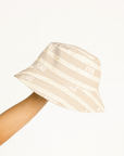 Beige and white striped bucket hat with 'FORE' branding held by a person on a white background