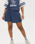 A person wearing a navy-colored knee-length skirt with a high waistband, paired with a golf club themed t-shirt and white sneakers.