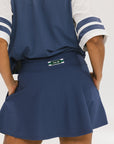 A person wearing a navy-colored knee-length skirt with a high waistband, paired with a golf club themed t-shirt and white sneakers.