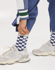 A person wearing indigo and white checkered Charlie Crew Socks with white sneakers and colorful pants.