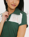 A woman wearing a color block green polo shirt with white front and back yoke detailing, paired with a white skirt.