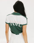 A woman wearing a color block green polo shirt with white front and back yoke detailing, paired with a white skirt.