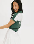 A woman wearing a color block green polo shirt with white front and back yoke detailing, paired with a white skirt.