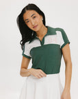 A woman wearing a color block green polo shirt with white front and back yoke detailing, paired with a white skirt.