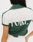 A woman wearing a color block green polo shirt with white front and back yoke detailing, paired with a white skirt.
