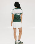 A woman wearing a color block green polo shirt with white front and back yoke detailing, paired with a white skirt.