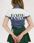 A woman wearing a color block indigo polo shirt with front and back yoke detailing, paired with a green skirt.