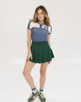 A woman wearing a color block indigo polo shirt with front and back yoke detailing, paired with a green skirt.