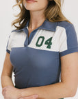 A woman wearing a color block indigo polo shirt with front and back yoke detailing, paired with a green skirt.