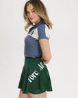 A person wearing a color block indigo polo shirt paired with a green skirt with text on it.