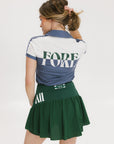 A woman wearing a color block indigo polo shirt with front and back yoke detailing, paired with a green skirt.