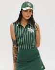 A female model wearing a sleeveless green pinstripe polo top with an applique logo on the chest and a matching green skirt, paired with a green cap.