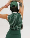 A female model wearing a sleeveless green pinstripe polo top with an applique logo on the chest and a matching green skirt, paired with a green cap.
