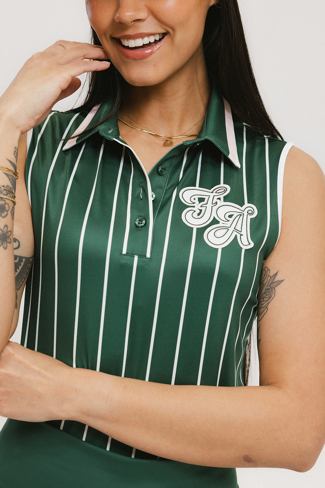 A female model wearing a sleeveless green pinstripe polo top with an applique logo on the chest.